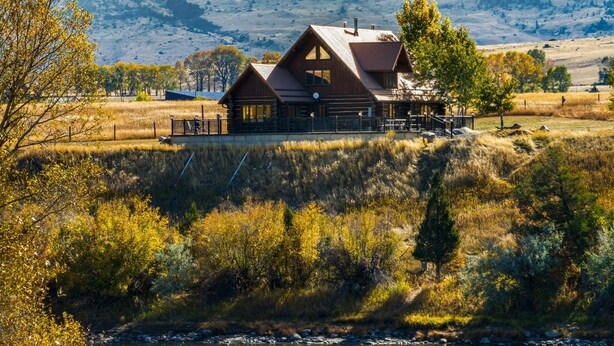 Une cabane en rondins dotée d’une grande véranda, située sur une colline surplombant une rivière.