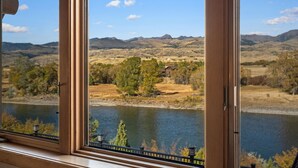 Une vue à travers une fenêtre sur une rivière, des collines et une maison au loin.