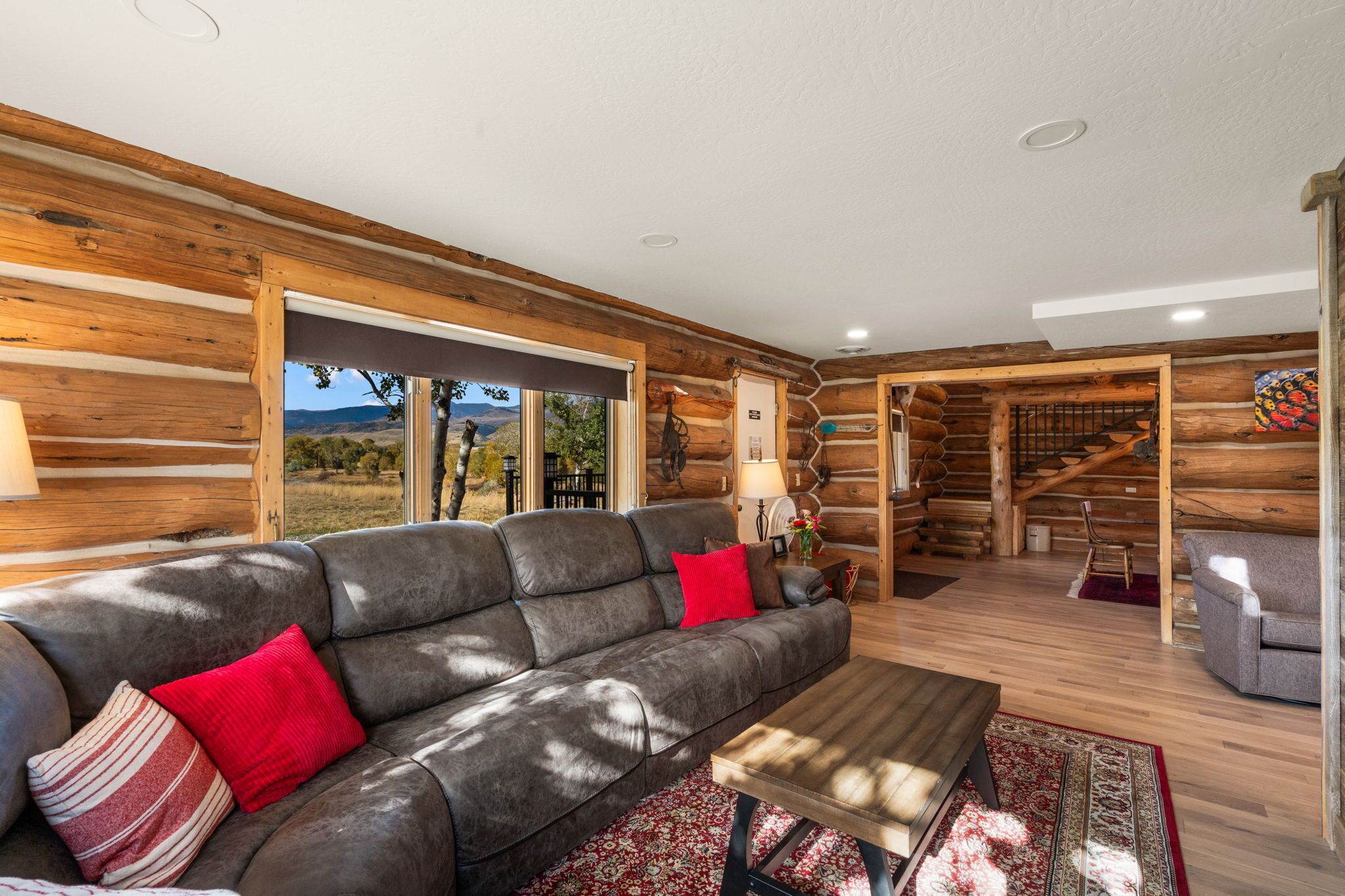 A log cabin interior with a leather sofa, a wooden coffee table, and a view of the outdoors.