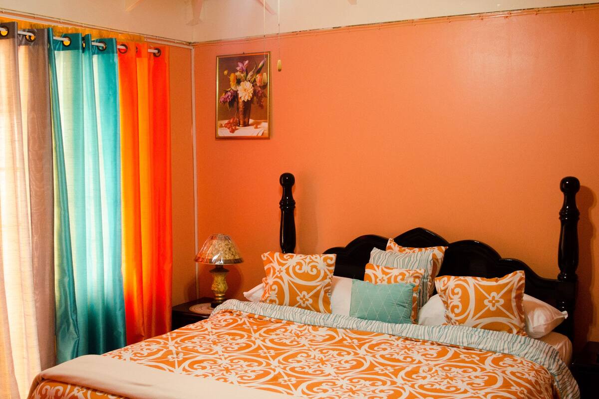 A bedroom with a bed, curtains, a ceiling fan, and a nightstand.