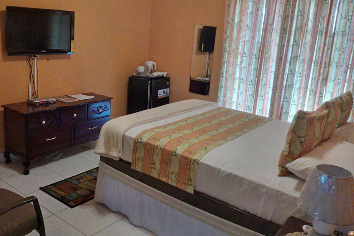 A hotel room with a bed, a television, a dresser, a refrigerator, and a window with curtains.