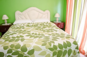 A bed with a leaf-patterned bedspread, two bedside tables with lamps, and a green wall.