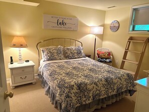 A bedroom with a bed, nightstand, lamp, chair, ladder, and a wall sign. - Charming Cottage Two Blocks from Downtown (Green Lake)