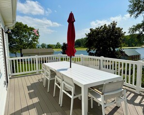 A deck with a white table and chairs, a red umbrella, and a view of a lake and trees. - Charming Cottage Two Blocks from Downtown (Green Lake)