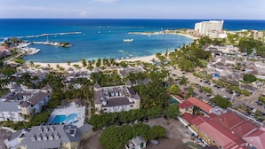 An aerial view of a coastal resort with a beach, marina, and hotel buildings.
