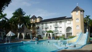 A pool area with a slide, palm trees, and a building with multiple balconies.