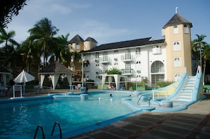 A pool area with a slide, palm trees, and a building with multiple balconies. - Conch Shell Studio at Sandcastles (Ocho Rios)