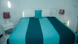 A neatly made bed with a teal and white striped bedspread, two white bedside tables with lamps, and a white headboard.