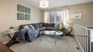 Ein modernes Wohnzimmer mit einem Ecksofa, einem Glastisch und einer Kronleuchter.