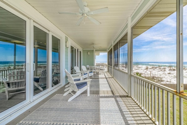 Ein überdachter Balkon mit weißen Stühlen und einem Tisch, mit Blick auf einen Strand.