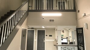 A multi-level interior with a staircase, doors labeled with room numbers, and a reception desk with a computer monitor.
