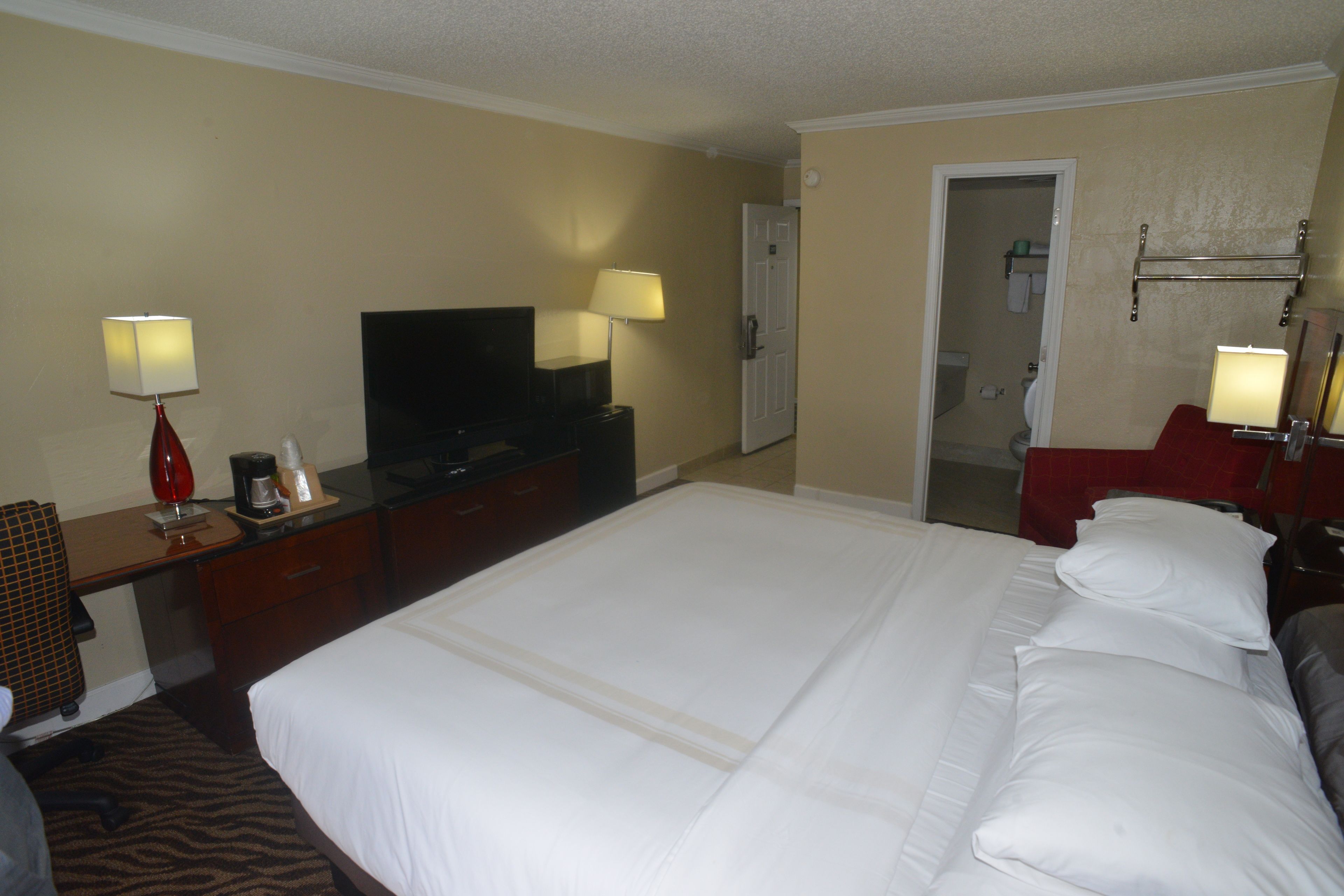 A hotel room with a large bed, a television, a desk with a lamp, and a bathroom visible through an open door.
