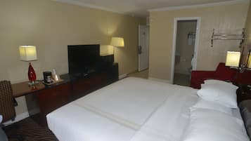 A hotel room with a large bed, a television, a desk with a lamp, and a bathroom visible through an open door.