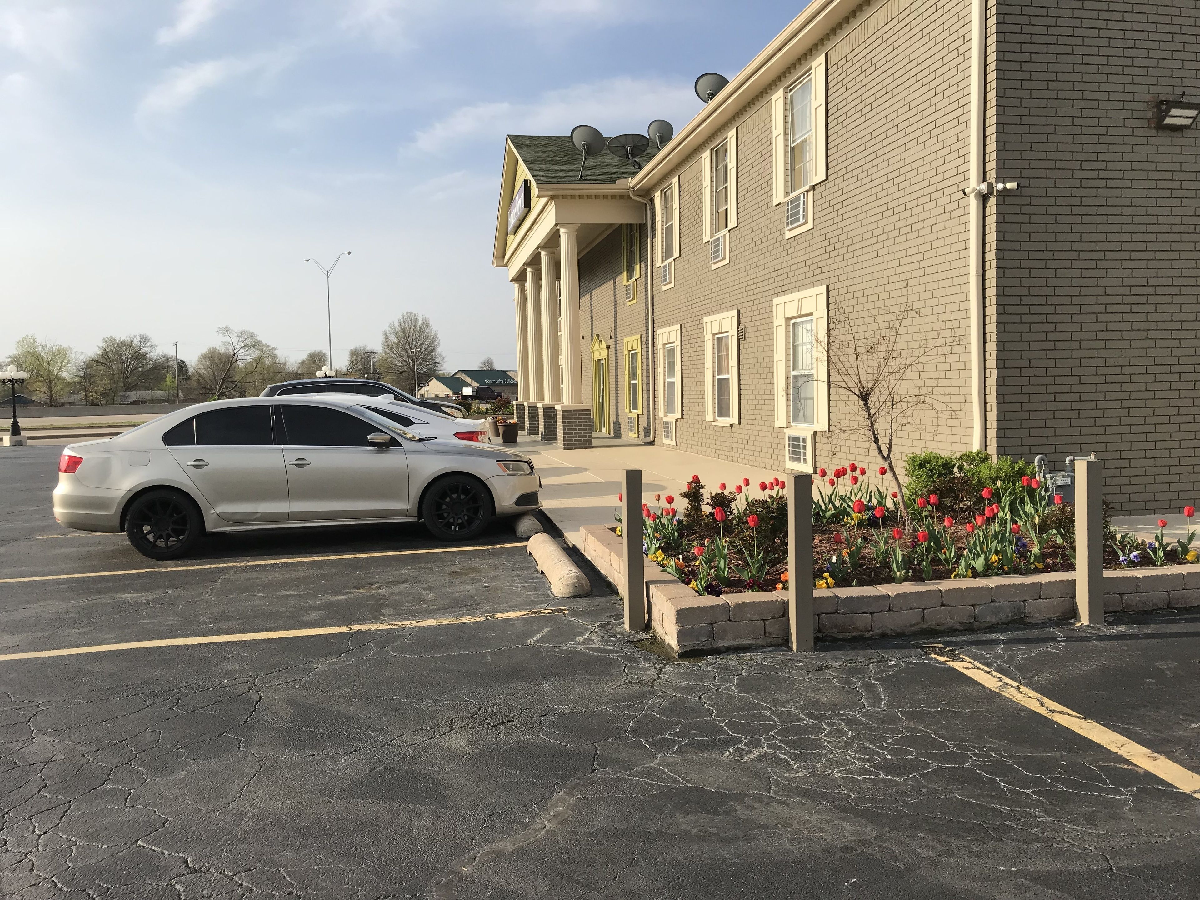 A parking lot with a white car parked near a building with multiple windows and satellite dishes on the roof.