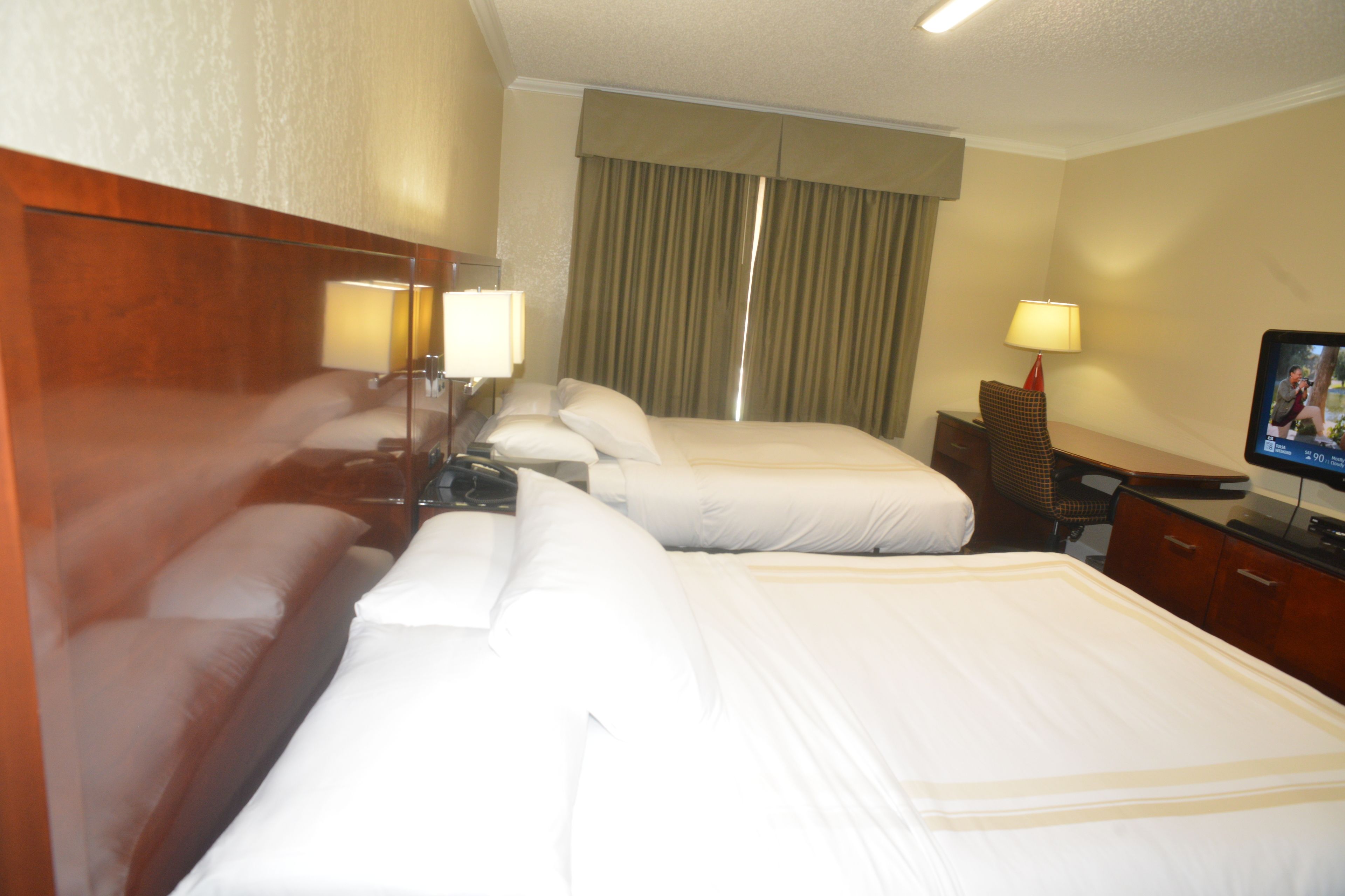 A hotel room with three beds, a desk, a chair, and a television.