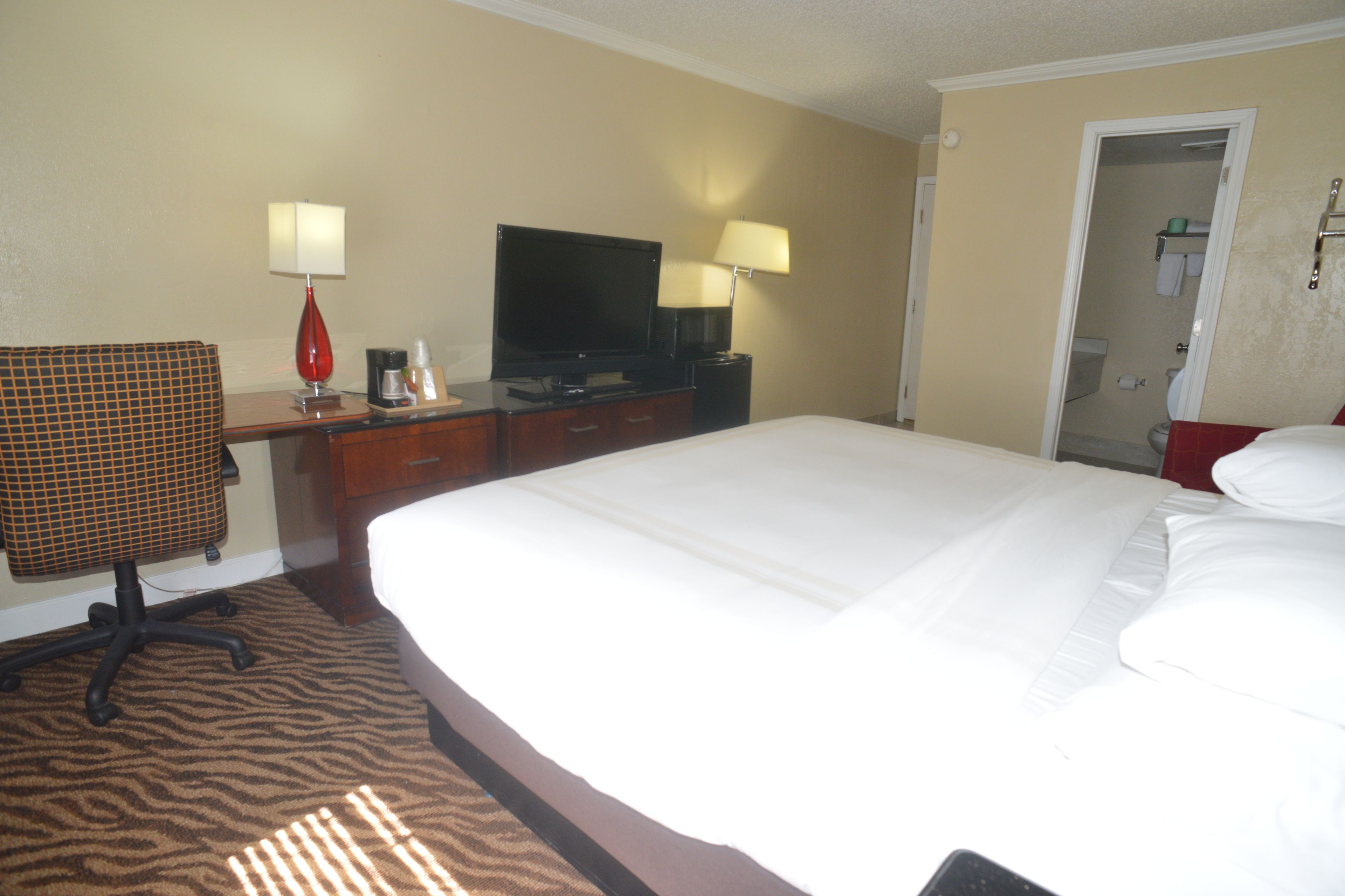 A hotel room with a large bed, a desk with a television, a chair, and a bathroom visible through an open door.