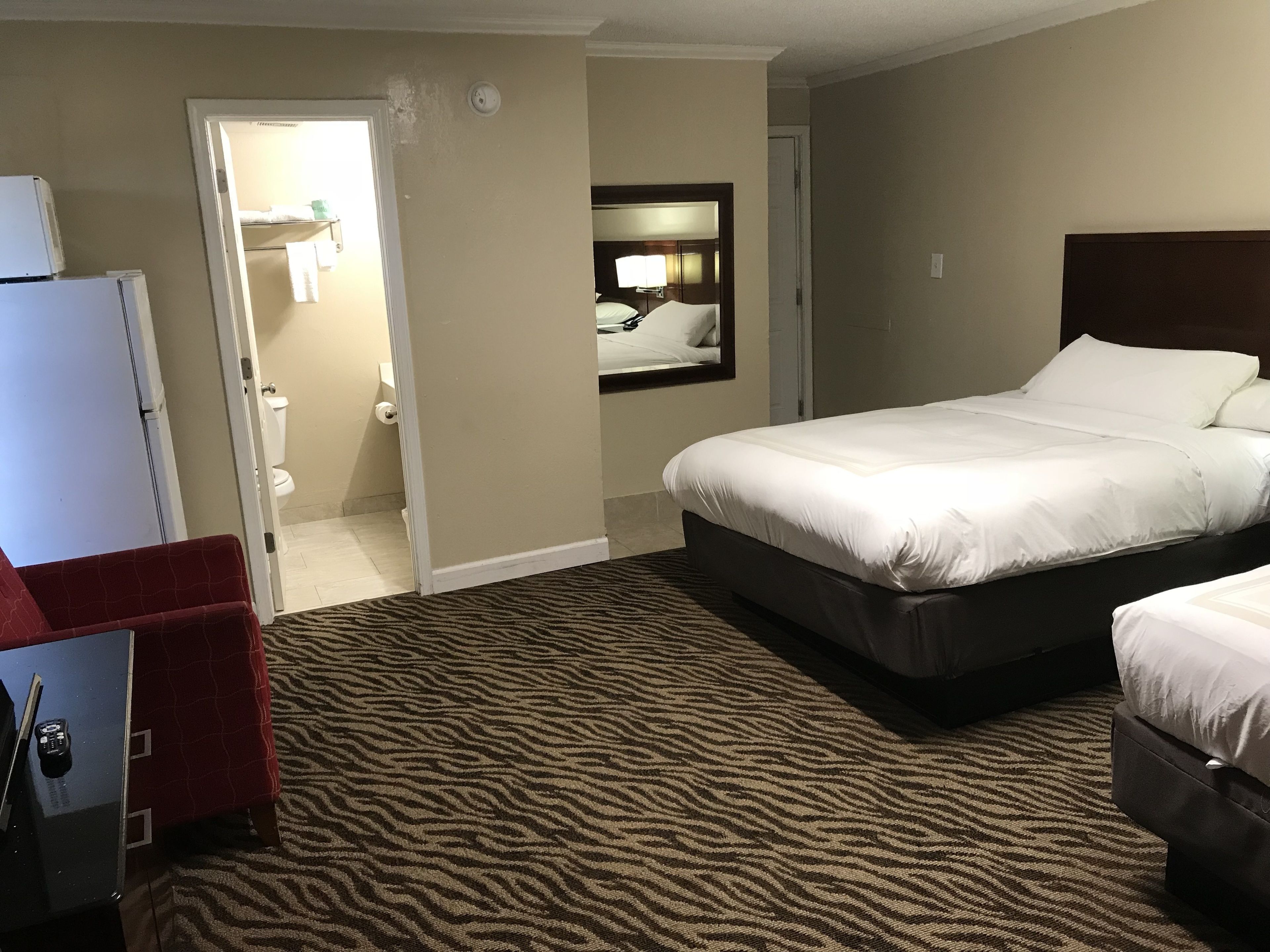 Ein Hotelzimmer mit einem großen Bett, einem Schreibtisch mit Stuhl, einem Kleiderständer und einem durchgegangene Tür erkennbaren Badezimmer.