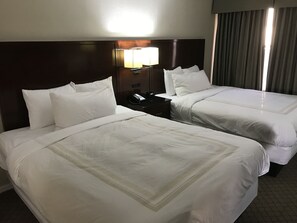 A hotel room with two beds, a nightstand with a phone, and a lamp.