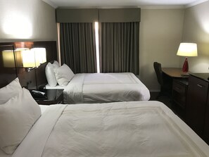 Quarto de hotel com duas camas, uma escrivaninha, uma cadeira, um abajur e um espelho.
