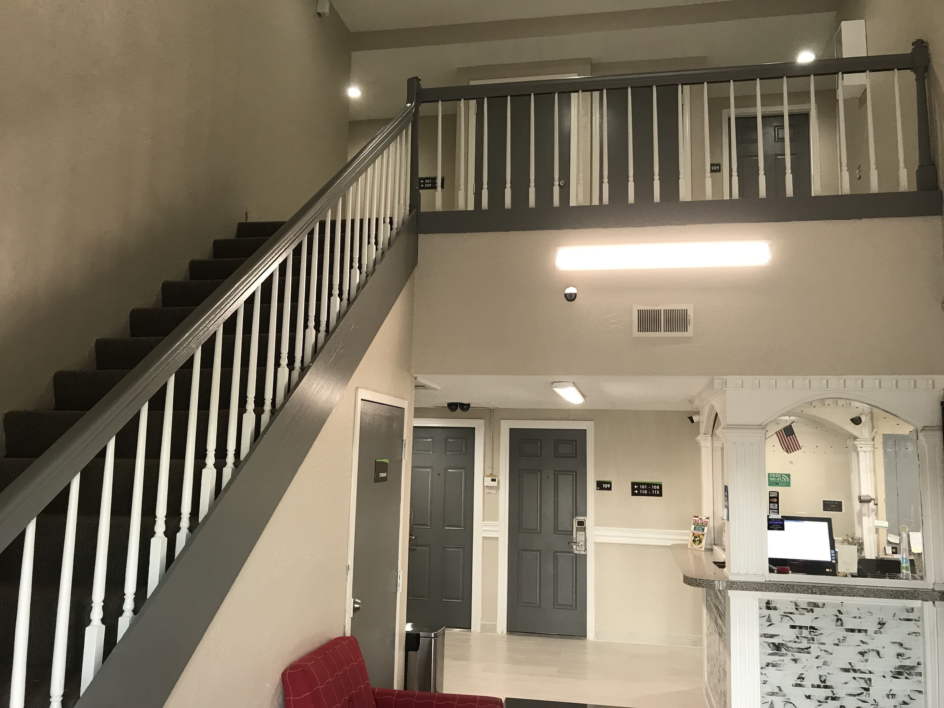 Un intérieur à plusieurs niveaux, avec un escalier, des portes portant l’indication du numéro de la pièce et un comptoir de réception équipé d’un écran d’ordinateur.