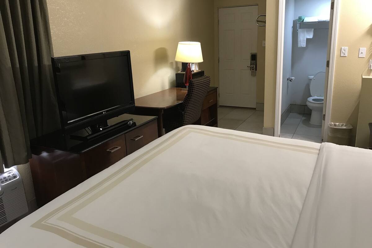 Une chambre d’hôtel avec un lit, une télévision, un bureau avec une lampe et une salle de bain visible à travers une porte ouverte.