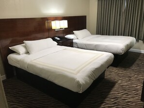 Een hotelkamer met twee bedden, een houten hoofdbord, een nachtkastje met een lamp en een kamerbreed tapijt met dessin.