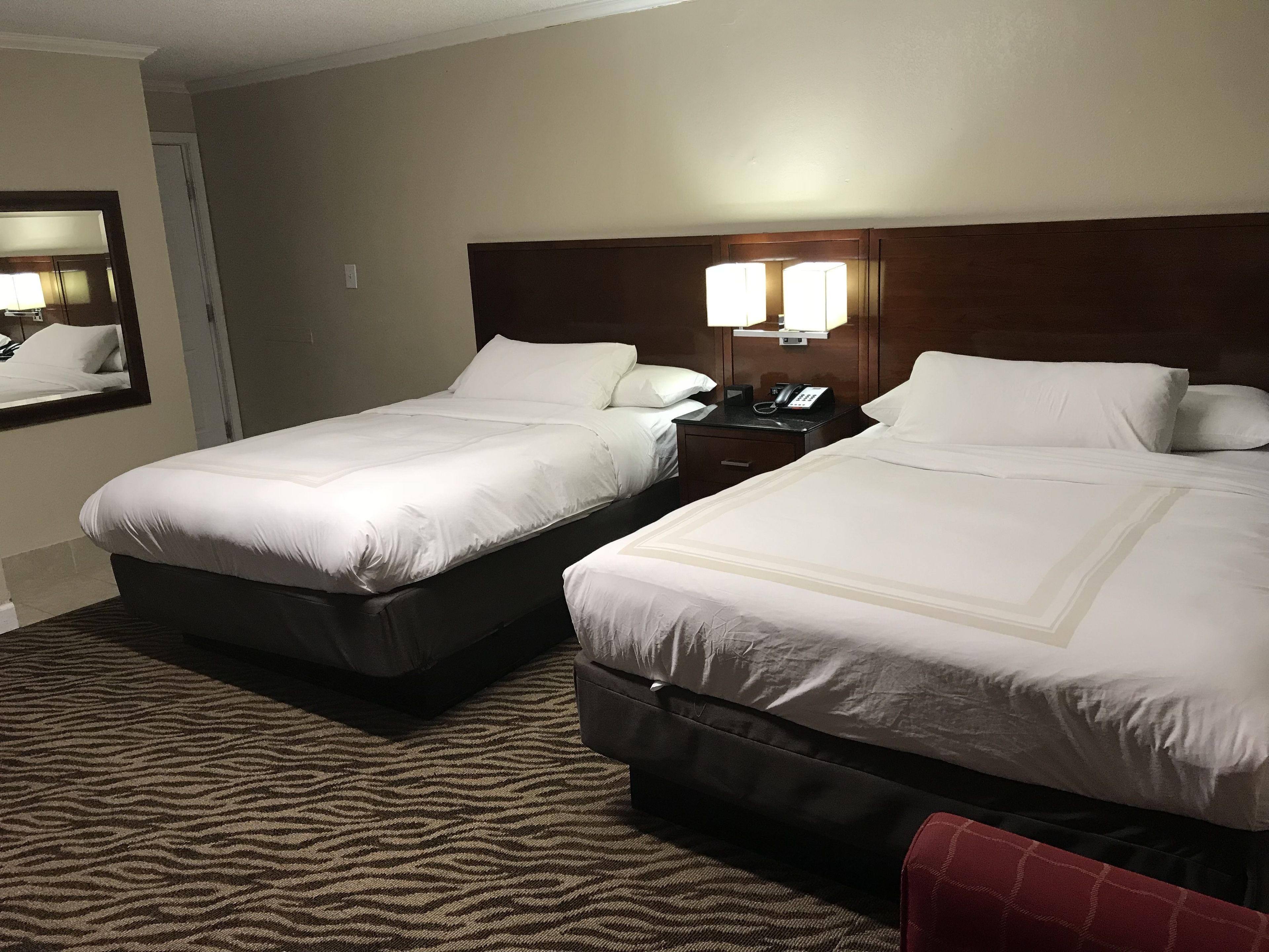 A hotel room with two beds, a nightstand with a lamp, and a carpeted floor.