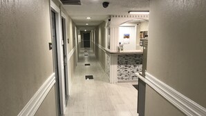 A hotel hallway with a tiled floor, a reception desk, and a door at the end.