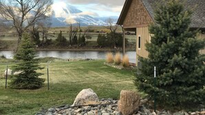 A lodge with a wooden exterior, a pond in the foreground, and mountains in the background. - Tranquil Home Along the Yellowstone River (Emigrant)