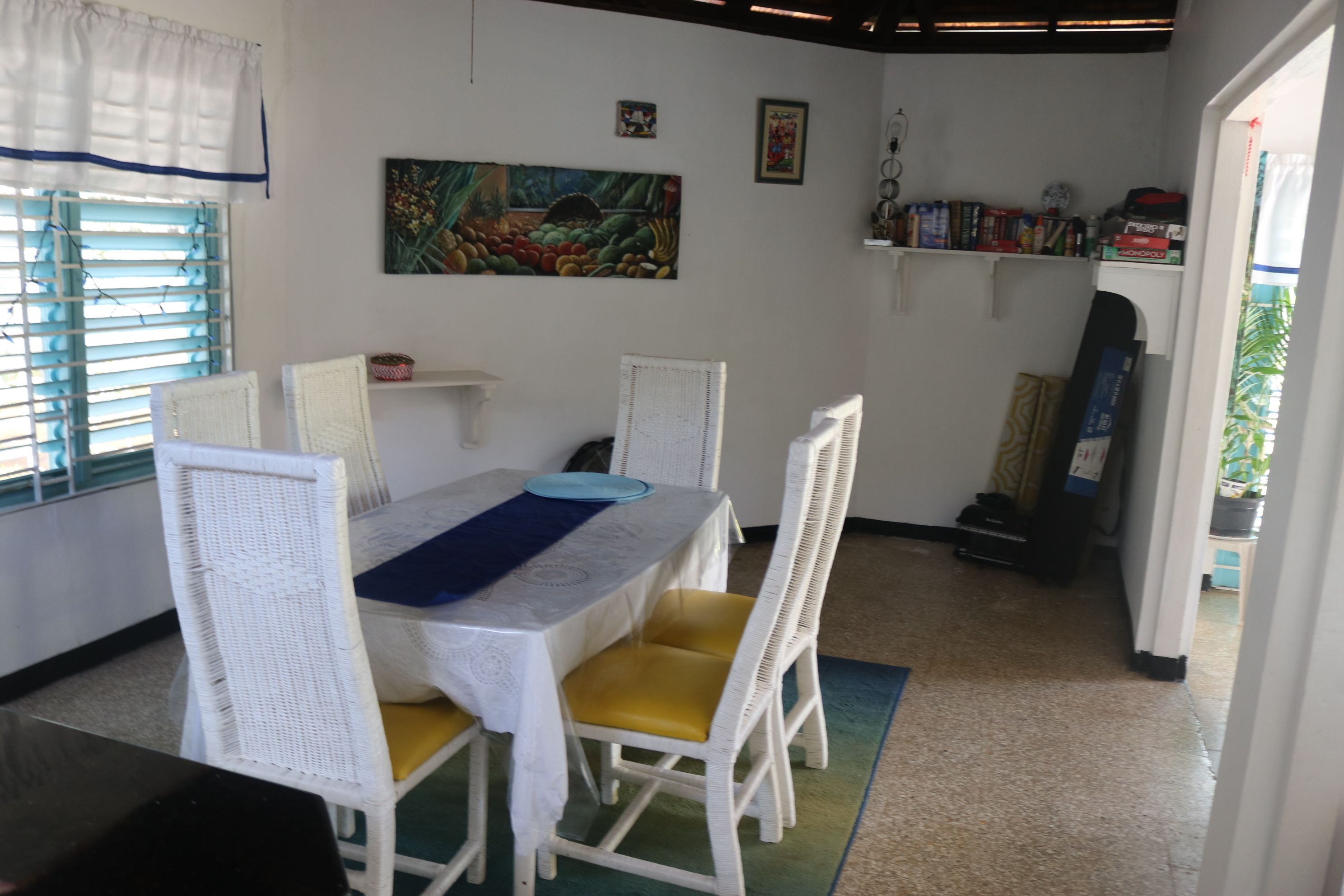 A dining area with a table and chairs, a painting on the wall, and shelves with items.
