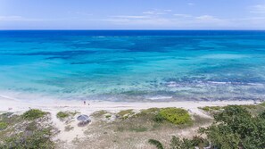 A beach with clear turquoise waters, a sandy shore, and some greenery in the foreground. - Beach Palm Villa (Duncans)