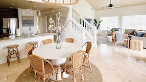 A spacious living area with a round dining table surrounded by wicker chairs, a chandelier, and a staircase leading to an upper level. - 3BR/3BA Villa: Central A/C! Short Walk To Beach! (Koloa)