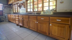 A kitchen with wooden cabinets, a sink, and a window with a view of trees. - Rainbow Hill (Negril)