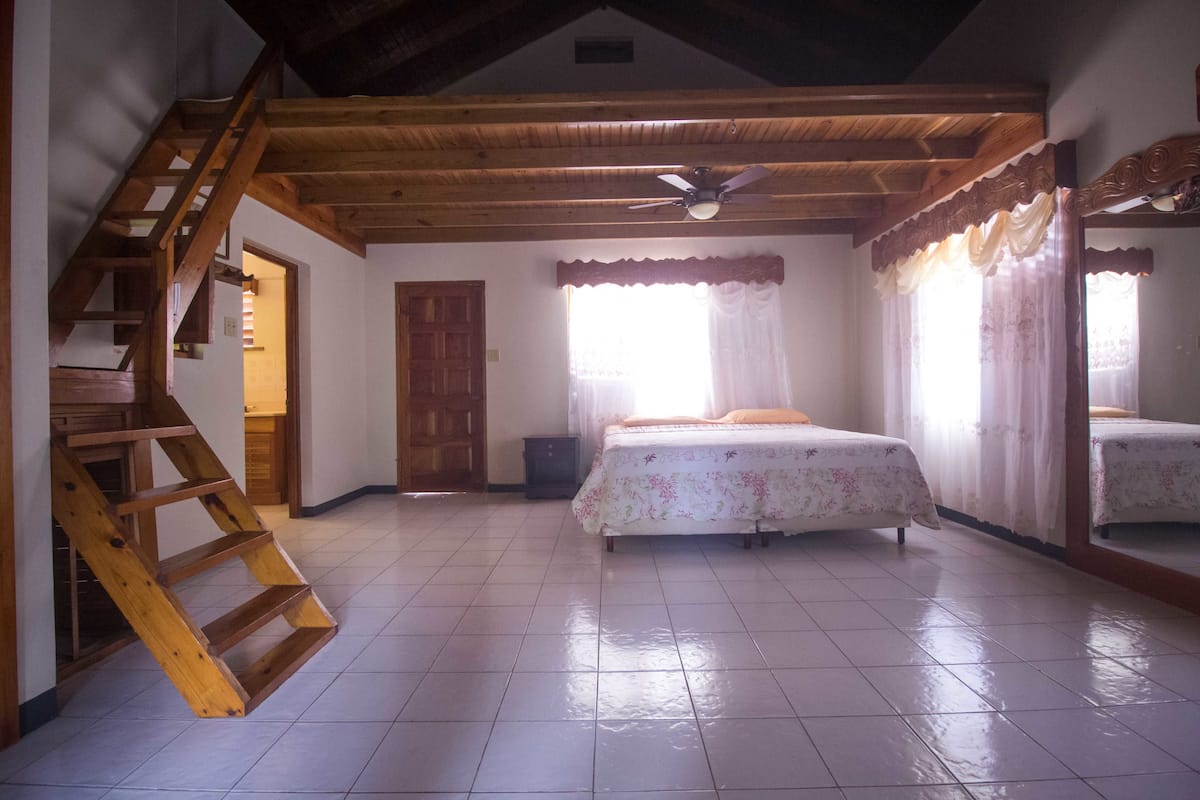 A bedroom with a wooden staircase, a bed with floral bedding, a ceiling fan, and a window with curtains.