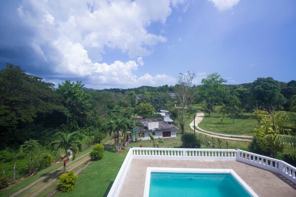 A pool with a white fence, surrounded by lush greenery and a house in the background. - Rainbow Hill (Negril)