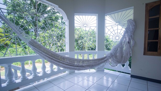 A hammock on a balcony with white railings and a view of trees. - Rainbow Hill (Negril)