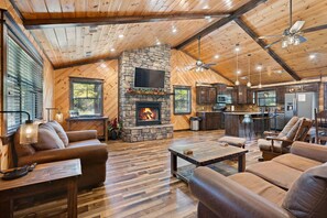 A spacious living area with a stone fireplace, leather sofas, and a wooden ceiling.