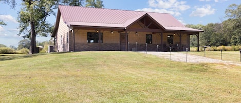 A rustic lodge with a metal roof and wooden walls, situated on a grassy hill with trees in the background.