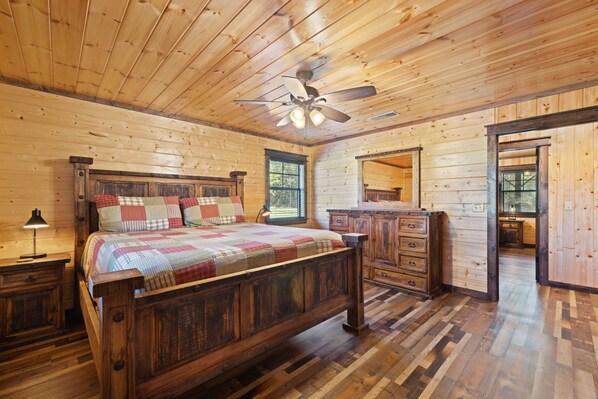 A wooden cabin bedroom with a bed, dresser, nightstand, and a ceiling fan.