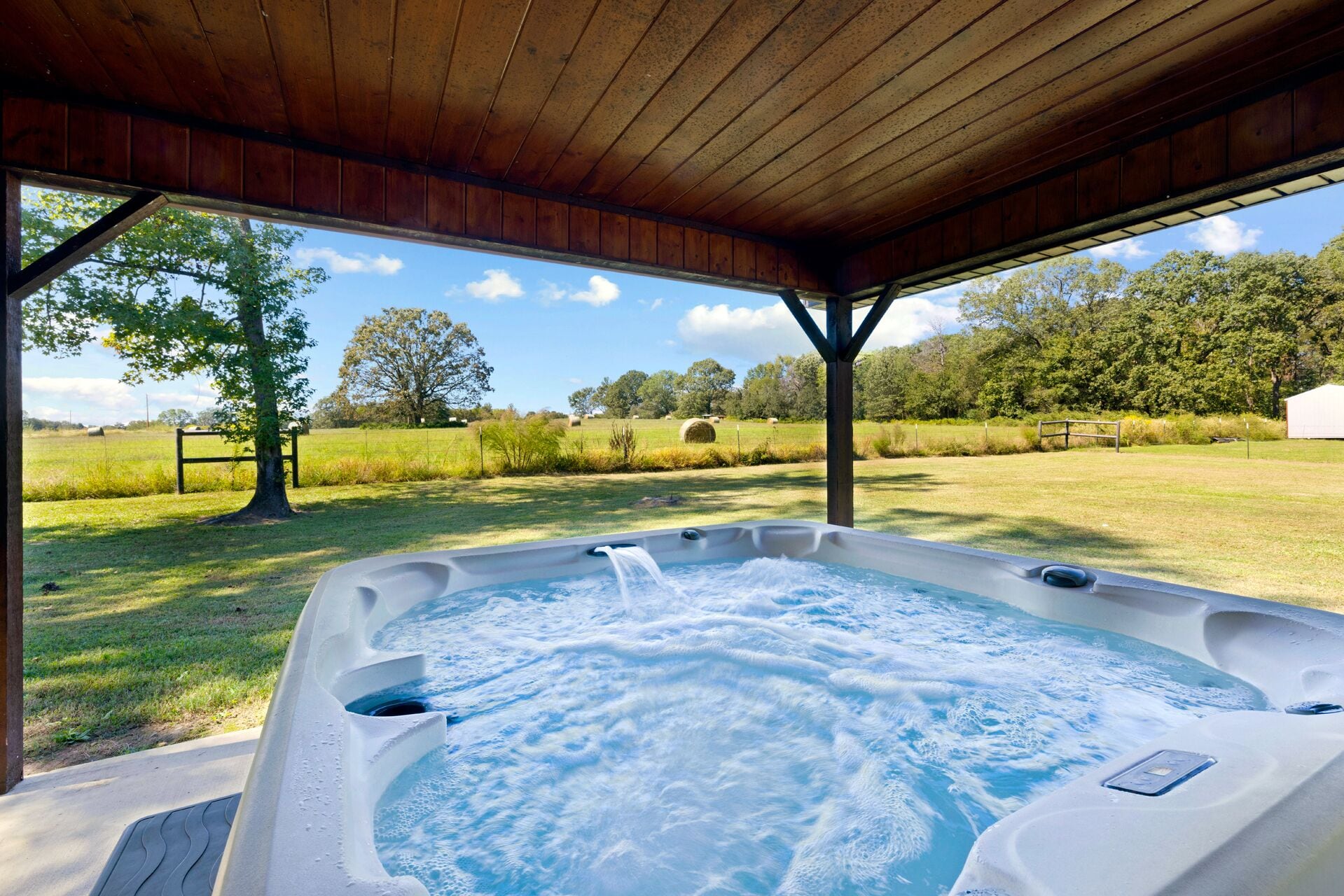 Een hottub onder een houten pergola met uitzicht op een gazon en bomen.