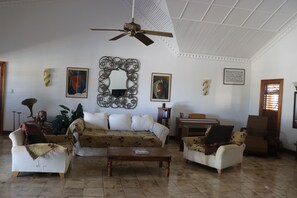 A spacious living room with a high ceiling, a ceiling fan, a large mirror, and several pieces of wall art.