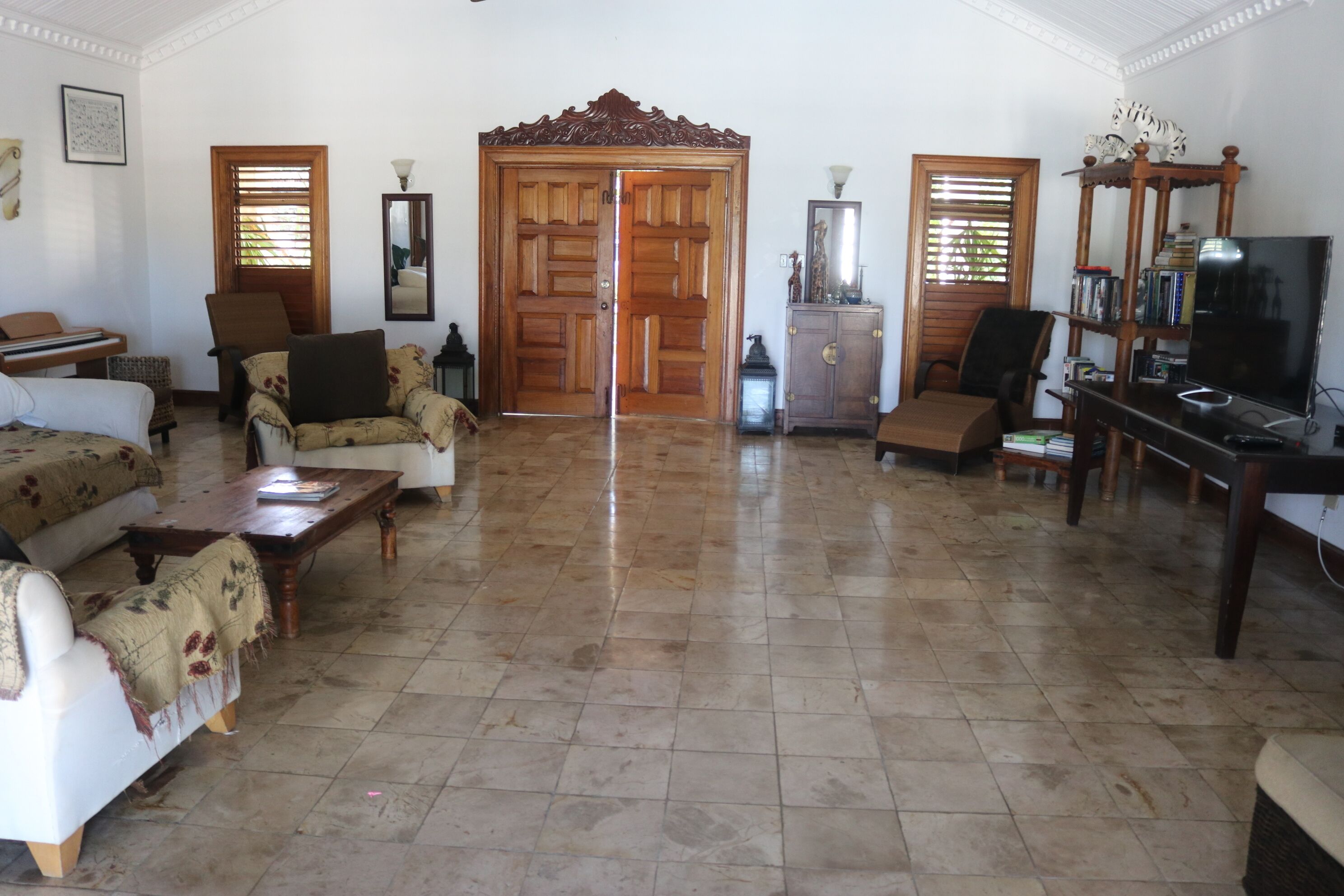 A spacious living room with a large wooden door, a television, and various seating options including a sofa and chairs.