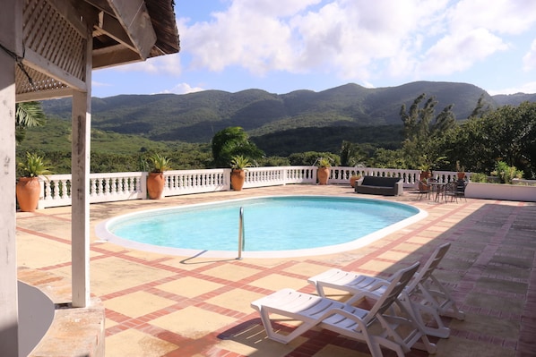 A pool area with a view of mountains, lounge chairs, and potted plants.