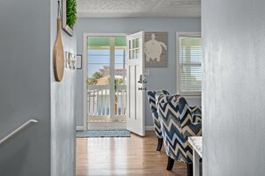 Un pasillo con una puerta de madera que da a un balcón, un comedor con sillas estampadas y una pared con cuadros enmarcados.