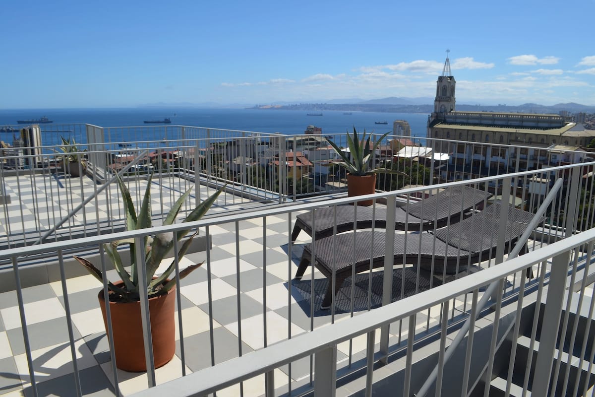 Terraço no telhado com piso xadrez, plantas em vasos e mobiliário de exterior.
