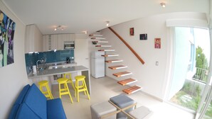A modern kitchen with a central island, yellow stools, a staircase with wooden steps, and a large sliding glass door leading to a balcony. - Lofts Plaza Yungay (Valparaiso)
