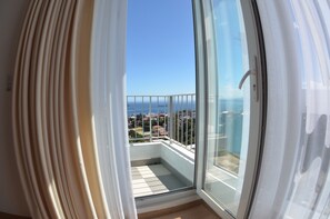 A balcony with a glass door, a view of the sea, and a cityscape in the background.