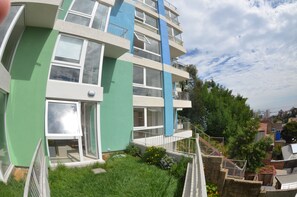 A multi-story residential building with balconies, large windows, and a green exterior.
