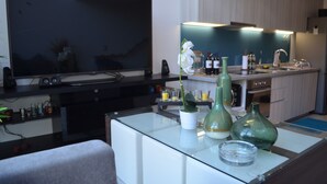 A modern kitchen with a flat-screen TV, a dining area with a glass table, and a kitchen counter with various items. - Lofts Plaza Yungay (Valparaiso)
