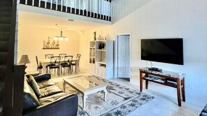A spacious living room with a high ceiling, a dining area, and a balcony with a railing.
